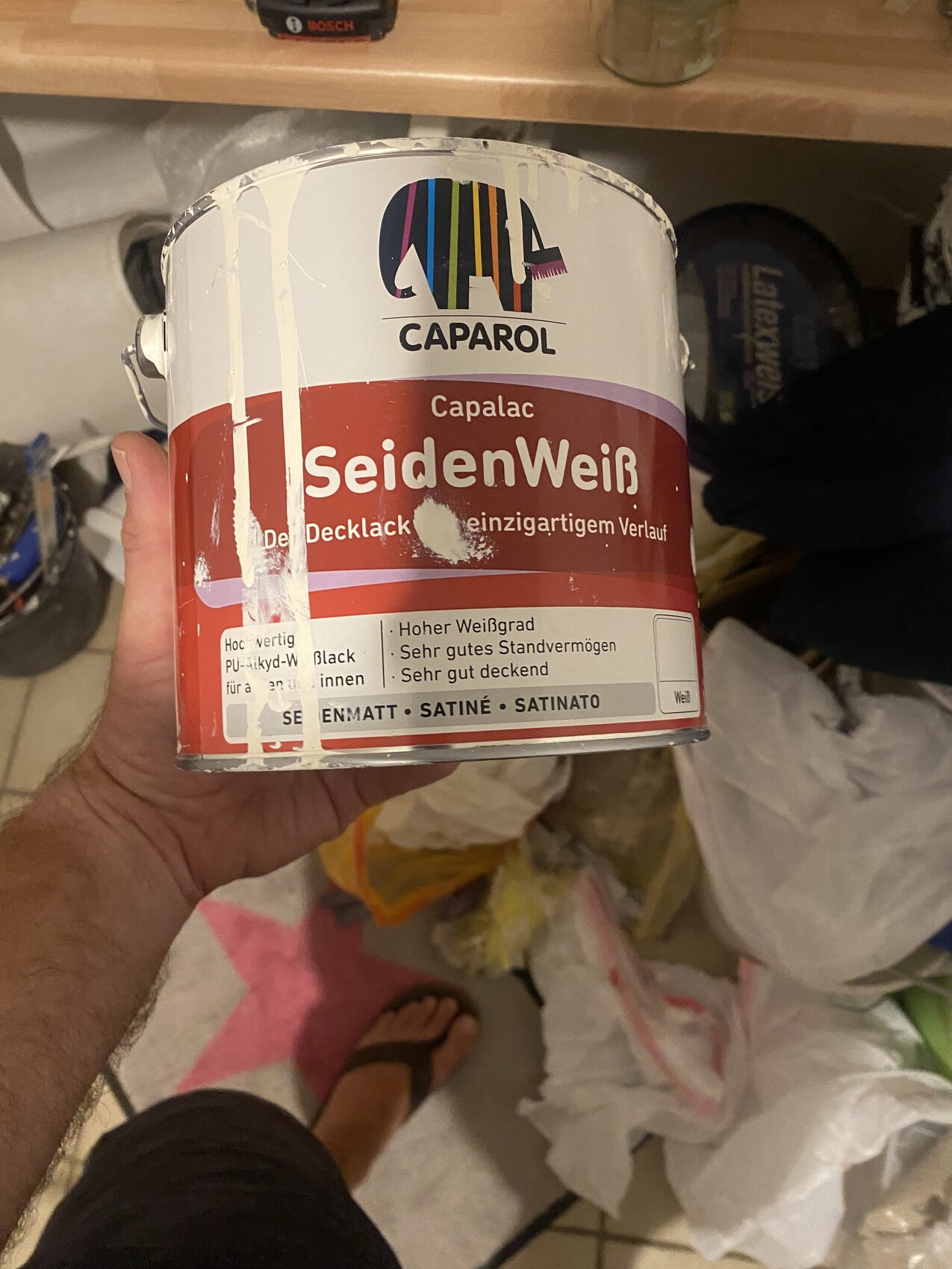 Person holds Caparol SeidenWeiß paint can (Capalac) in a workshop.
