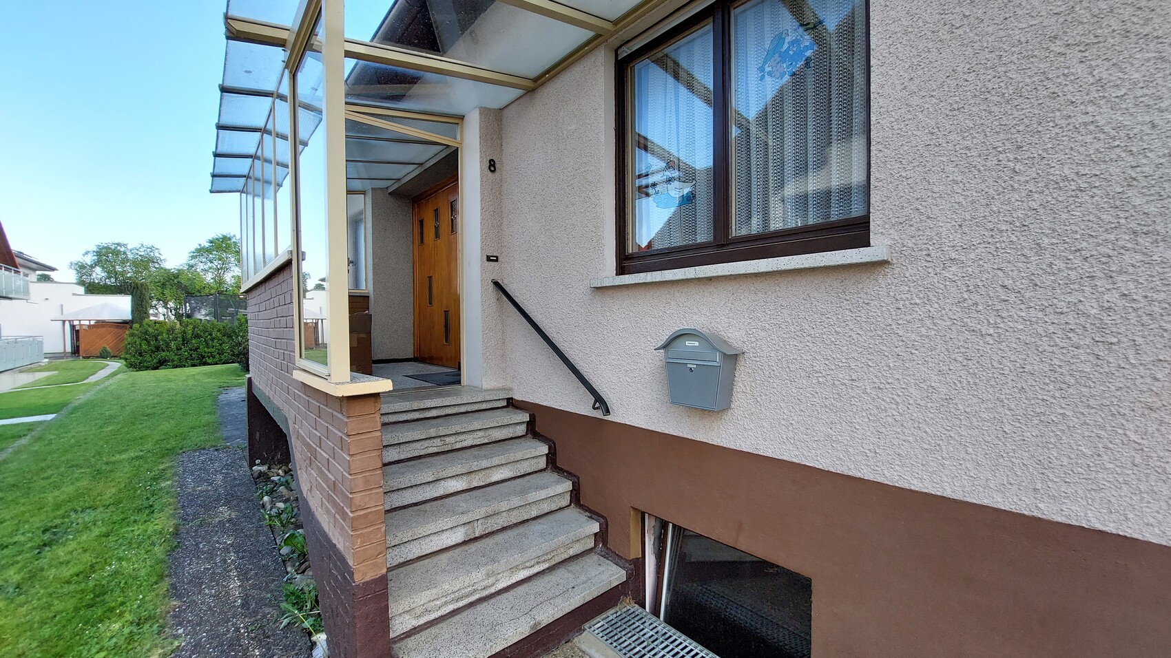 Exterior entrance of a residential house: stairs, railing, door No. 8, mailbox and window with curtains.