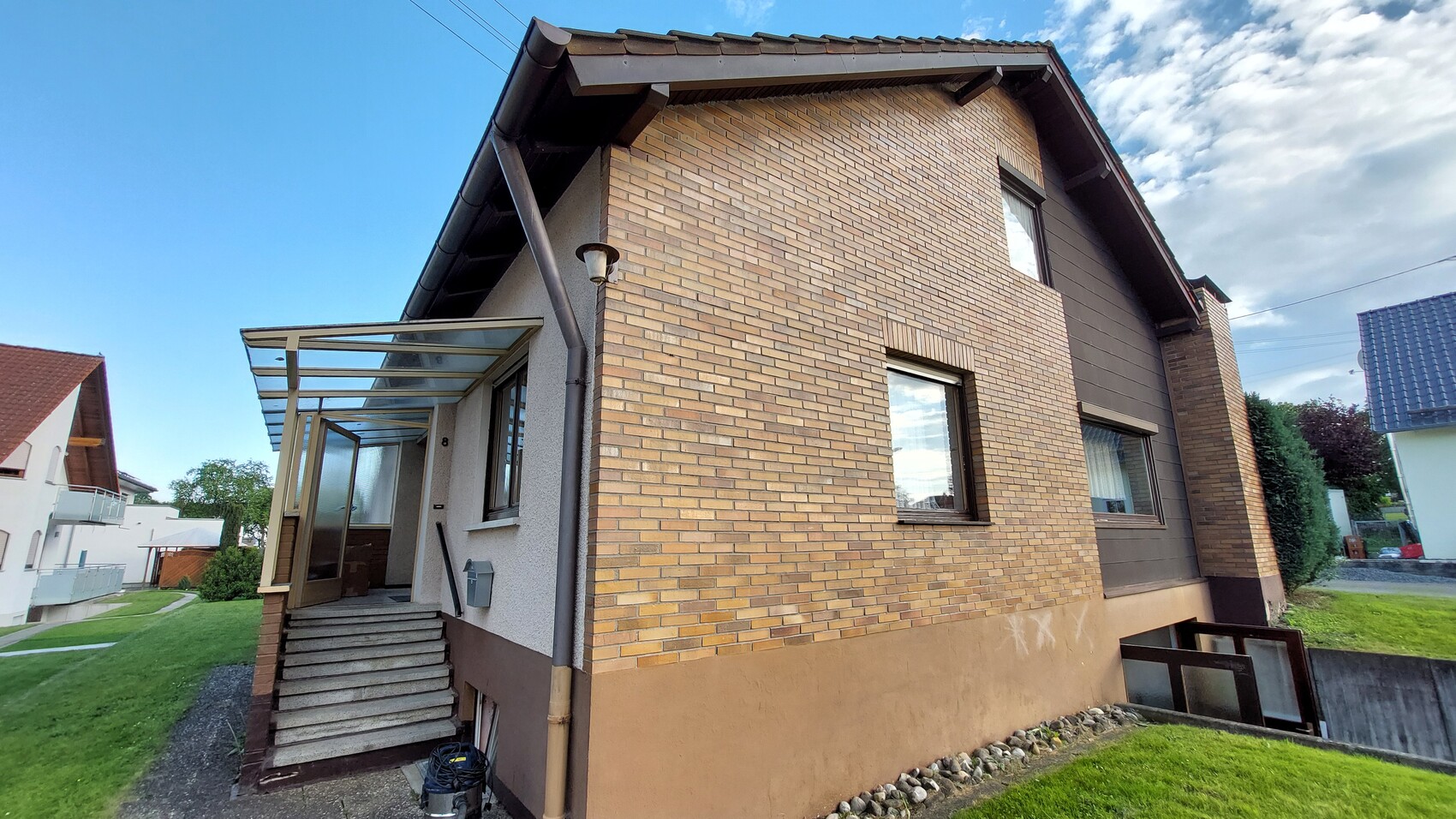 Exterior view of a two-story house with yellow-brown clinker brick walls, stairs and glass porch roof