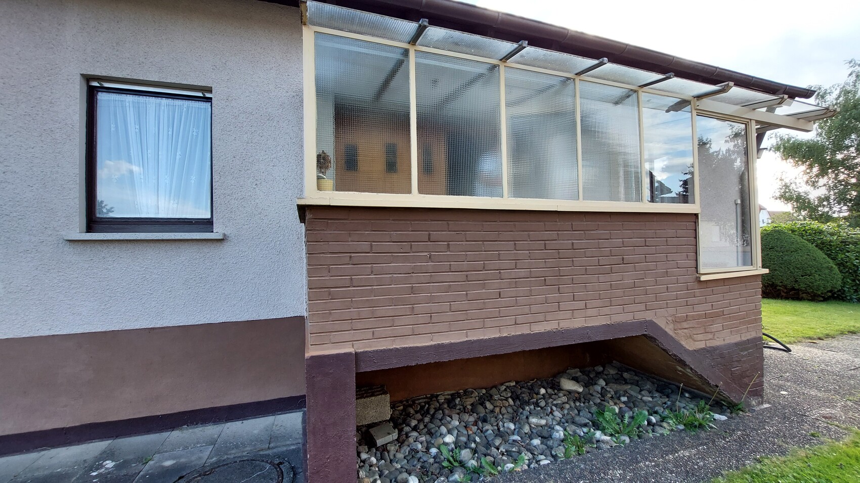 Exterior view of a house with glazed veranda/winter garden, brown brick wall and garden.