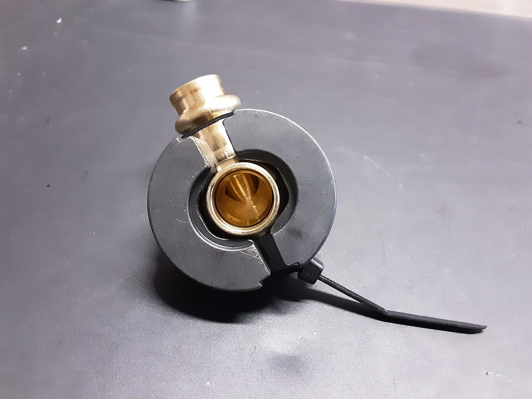 Round grey metal housing with central golden bearing, upper bolt, black cable
