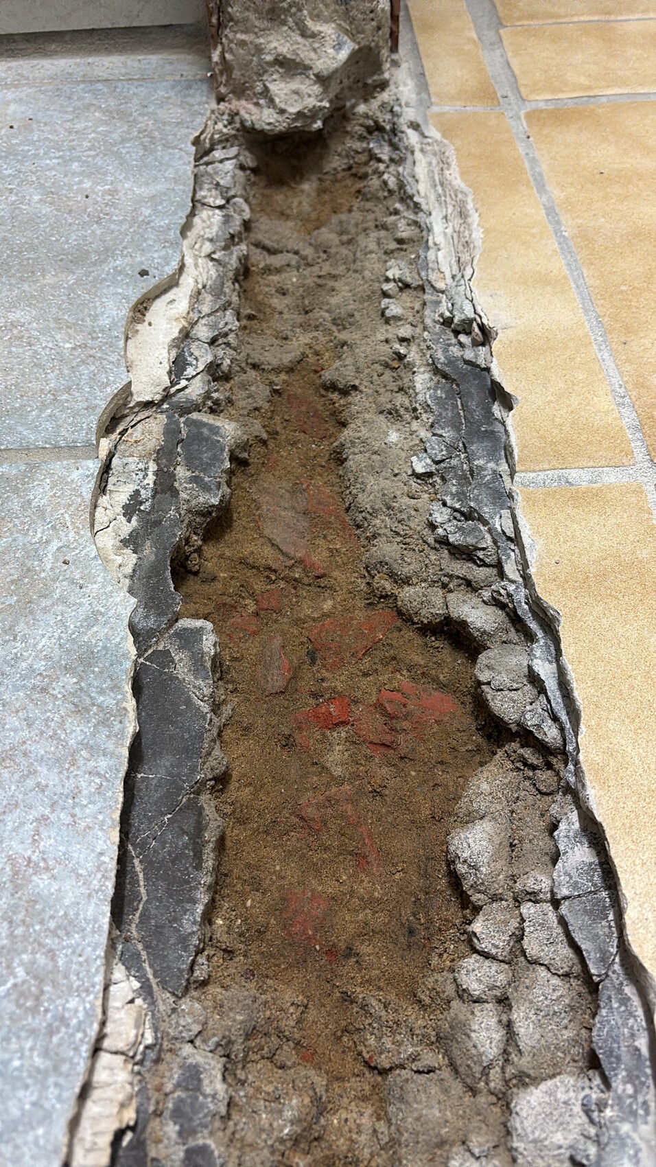 Offene Bodenspalte mit Sand und Bruchstücken zerbrochener Fliesen in einem Fliesenbodenbereich