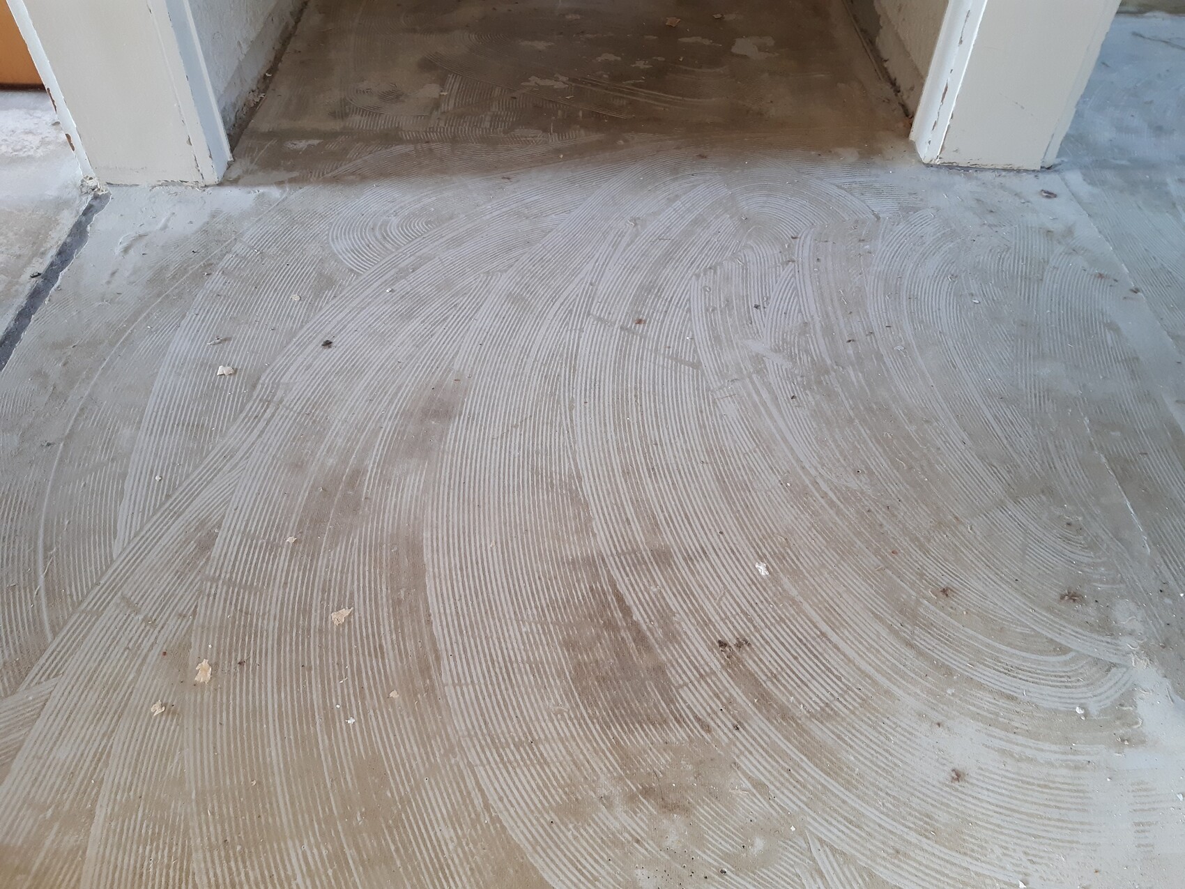 Concrete floor in the entrance area with circular grinding marks and dust.
