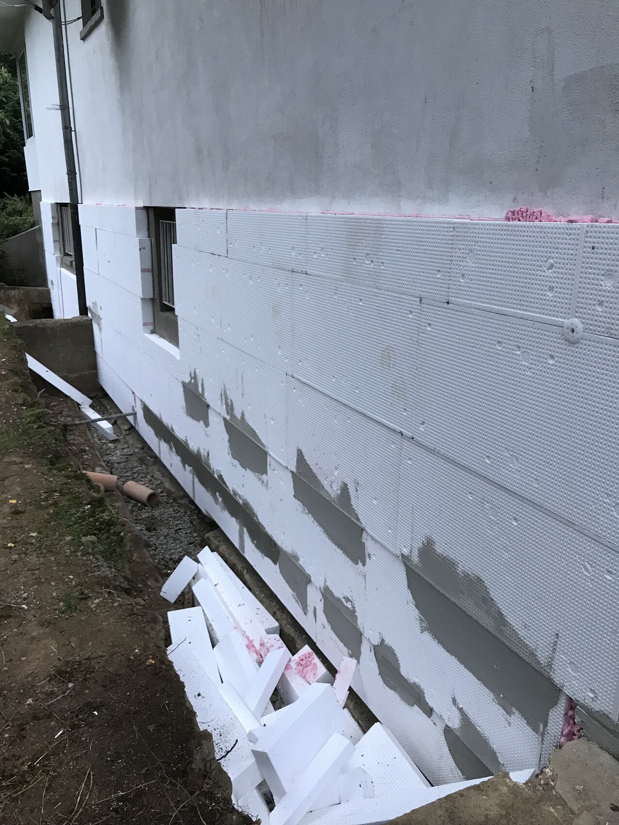 Außenwand eines Hauses mit weißer Styropor-Dämmung; Bauabbruchreste am Boden.