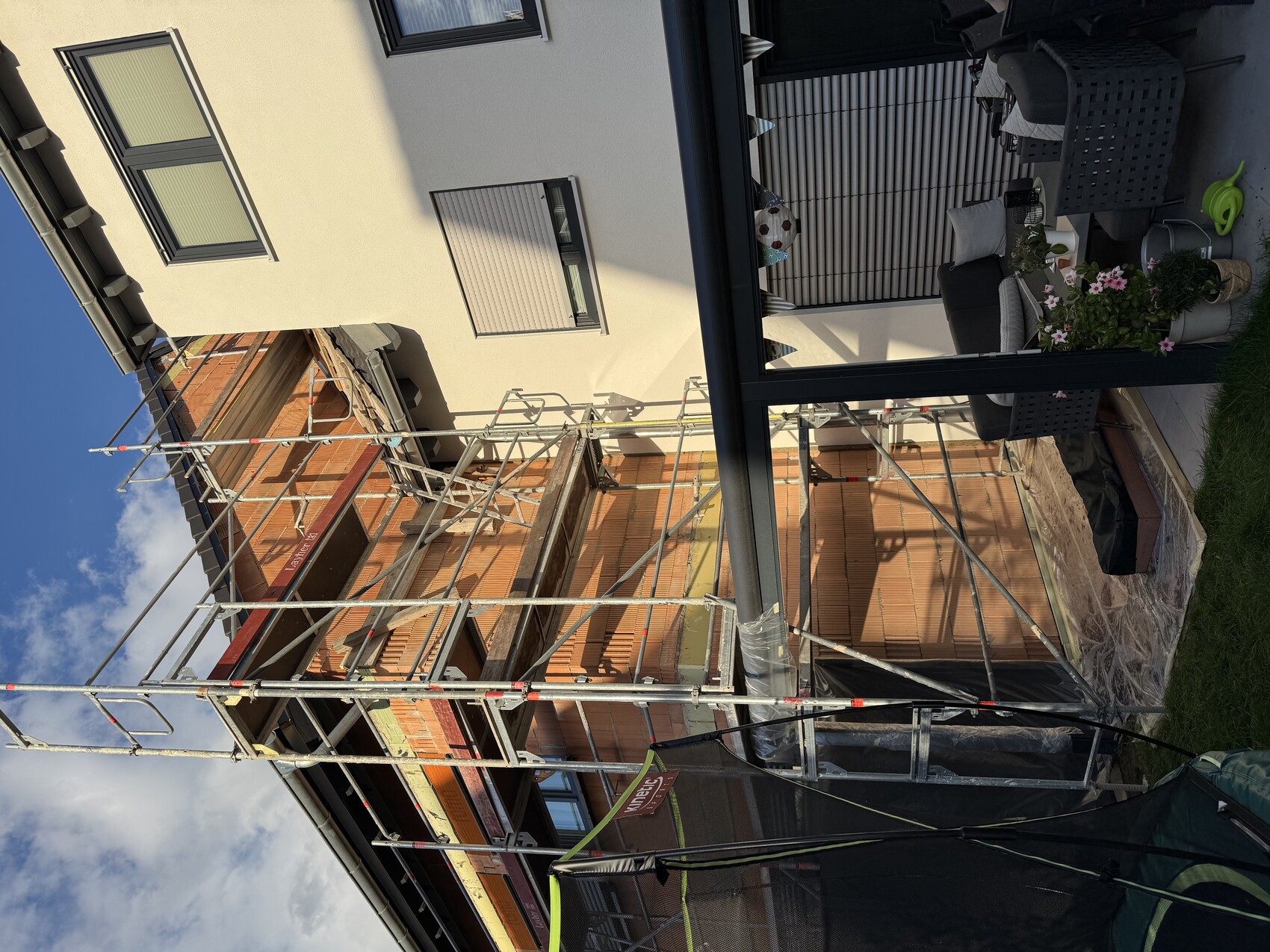 Scaffolding around new brick extension, adjoining facade; garden area with seating.