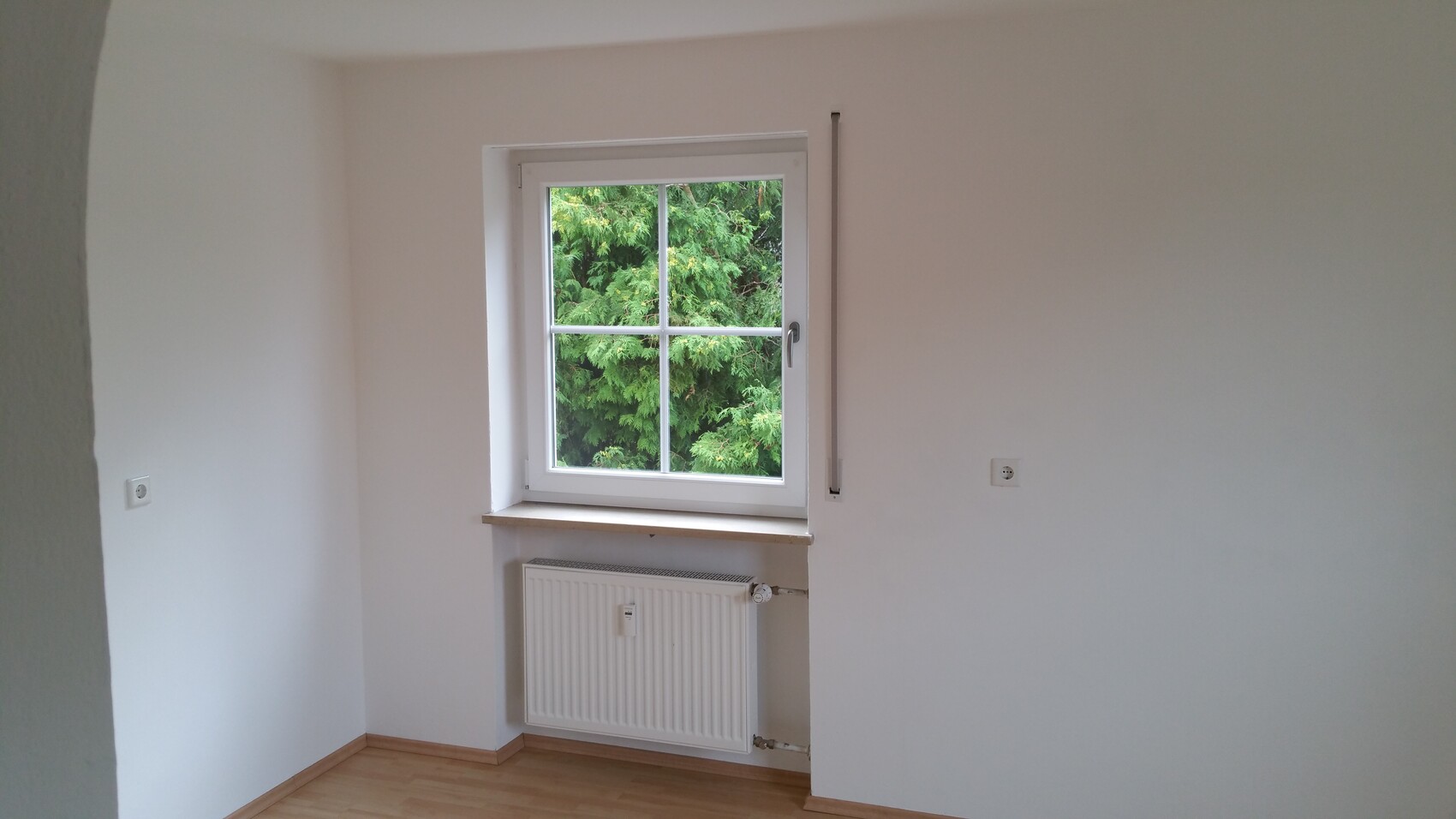 Small room with white window, radiator below, view of green trees