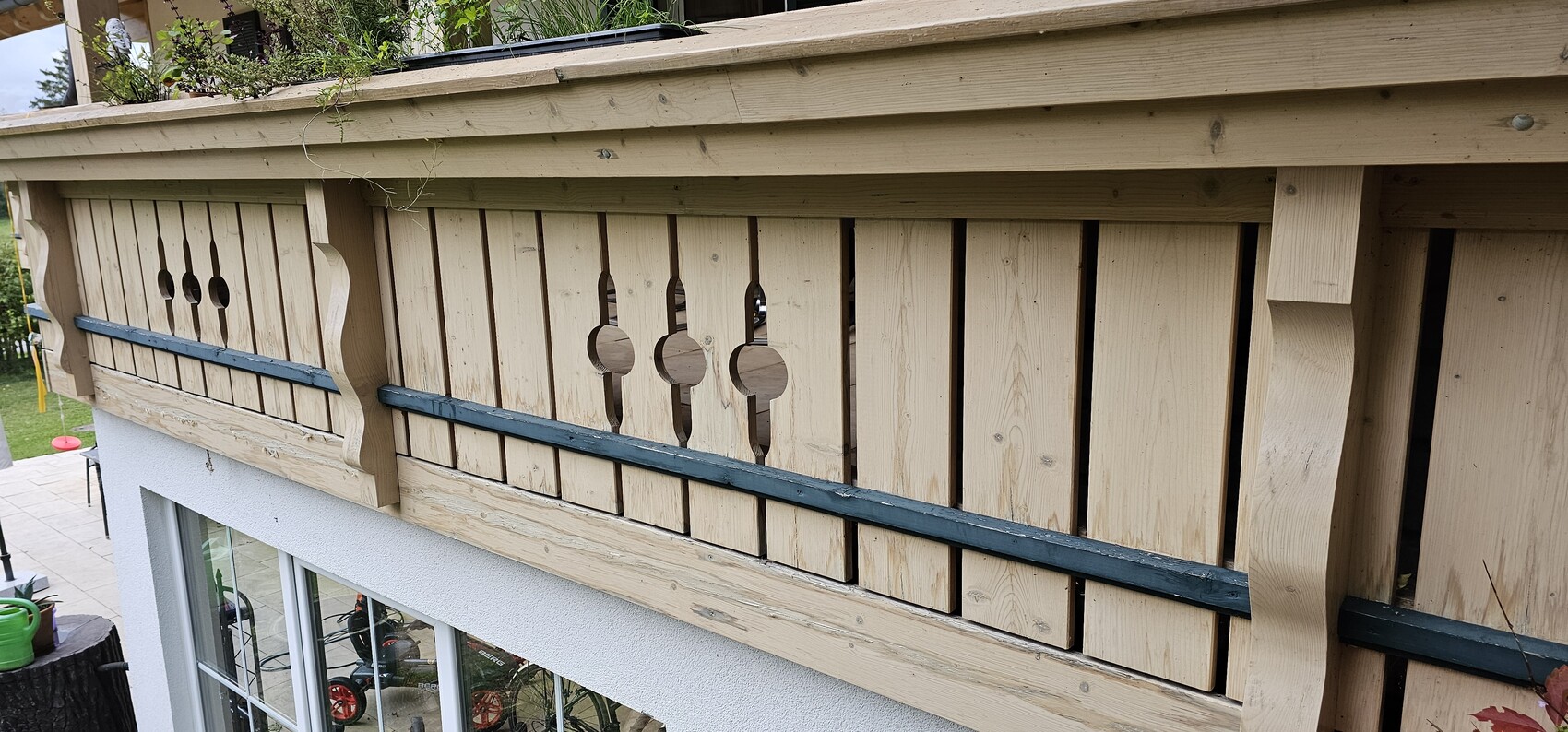 Wooden balcony railing with vertical slats, round openings, and blue trim.