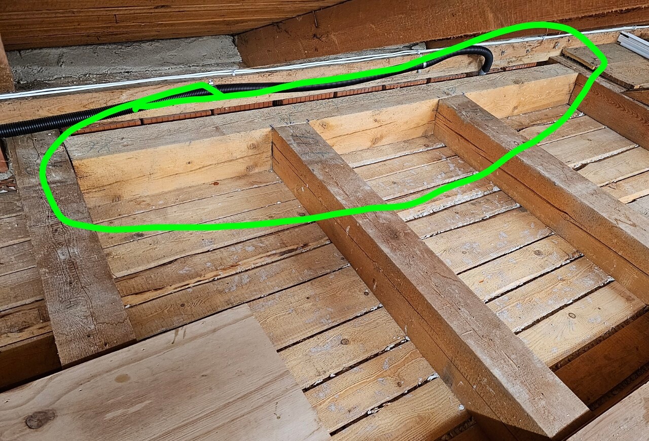 Dachboden mit Holzbalken; schwarzes Kabel verläuft entlang der oberen Kante, daneben weiße Leitung