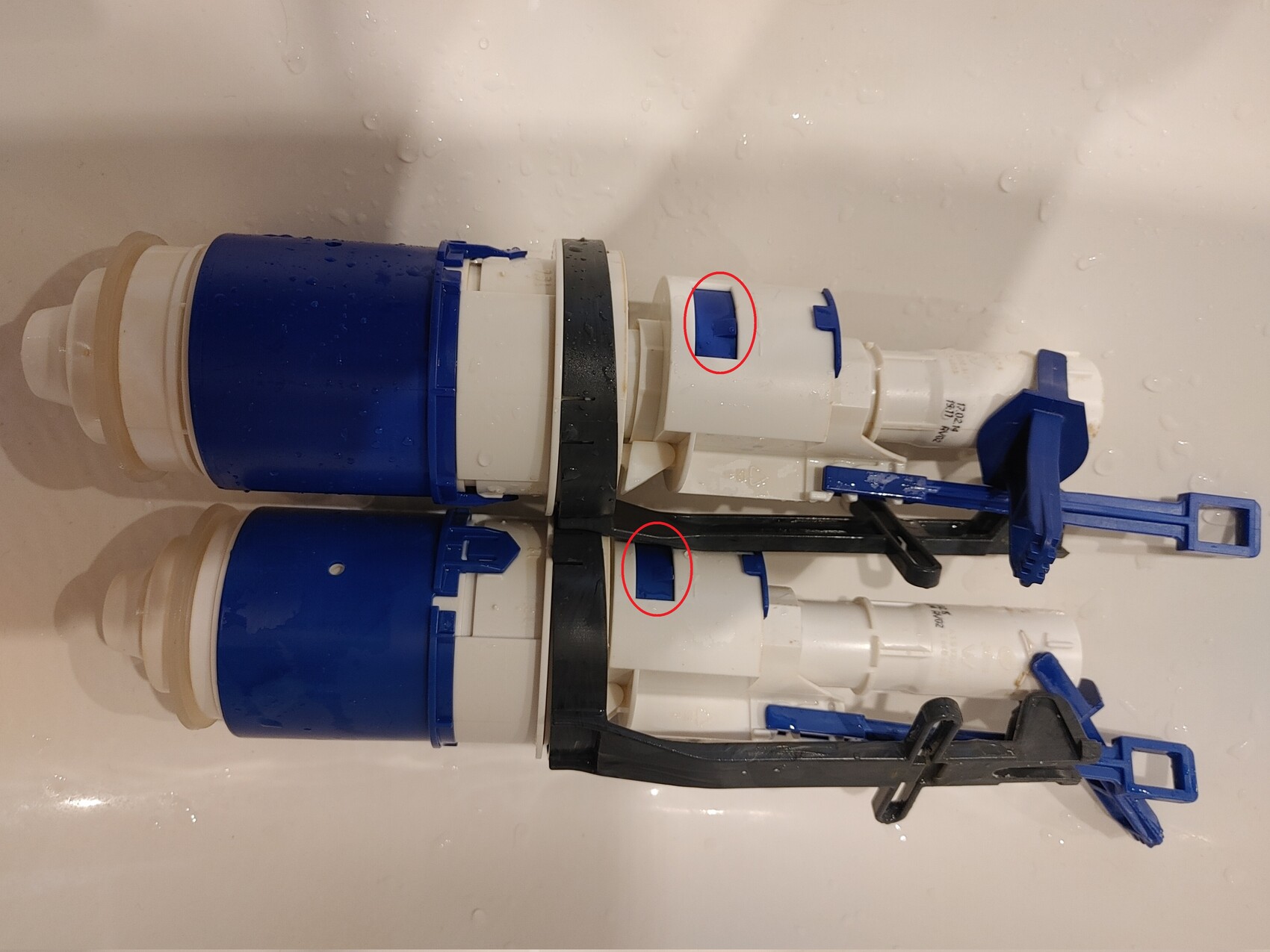Two white plastic flush valve blocks with blue handles, part of a toilet cistern.