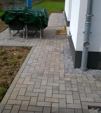 Paved terrace at the residential building with garden area and covered outdoor furniture.