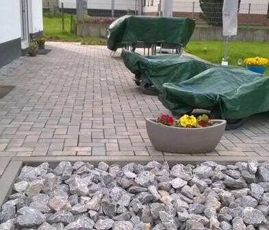 Paved terrace with stone slabs, garden furniture covered in green, and flower pots.