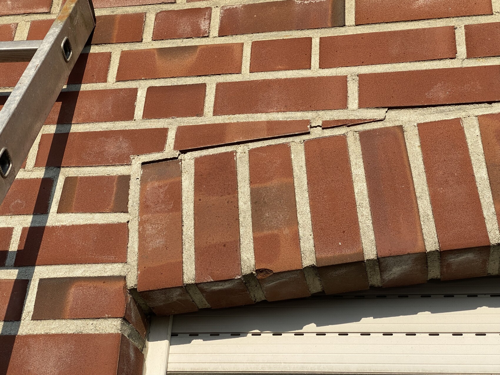 Exterior wall of red brick with ladder and roller shutter at bottom