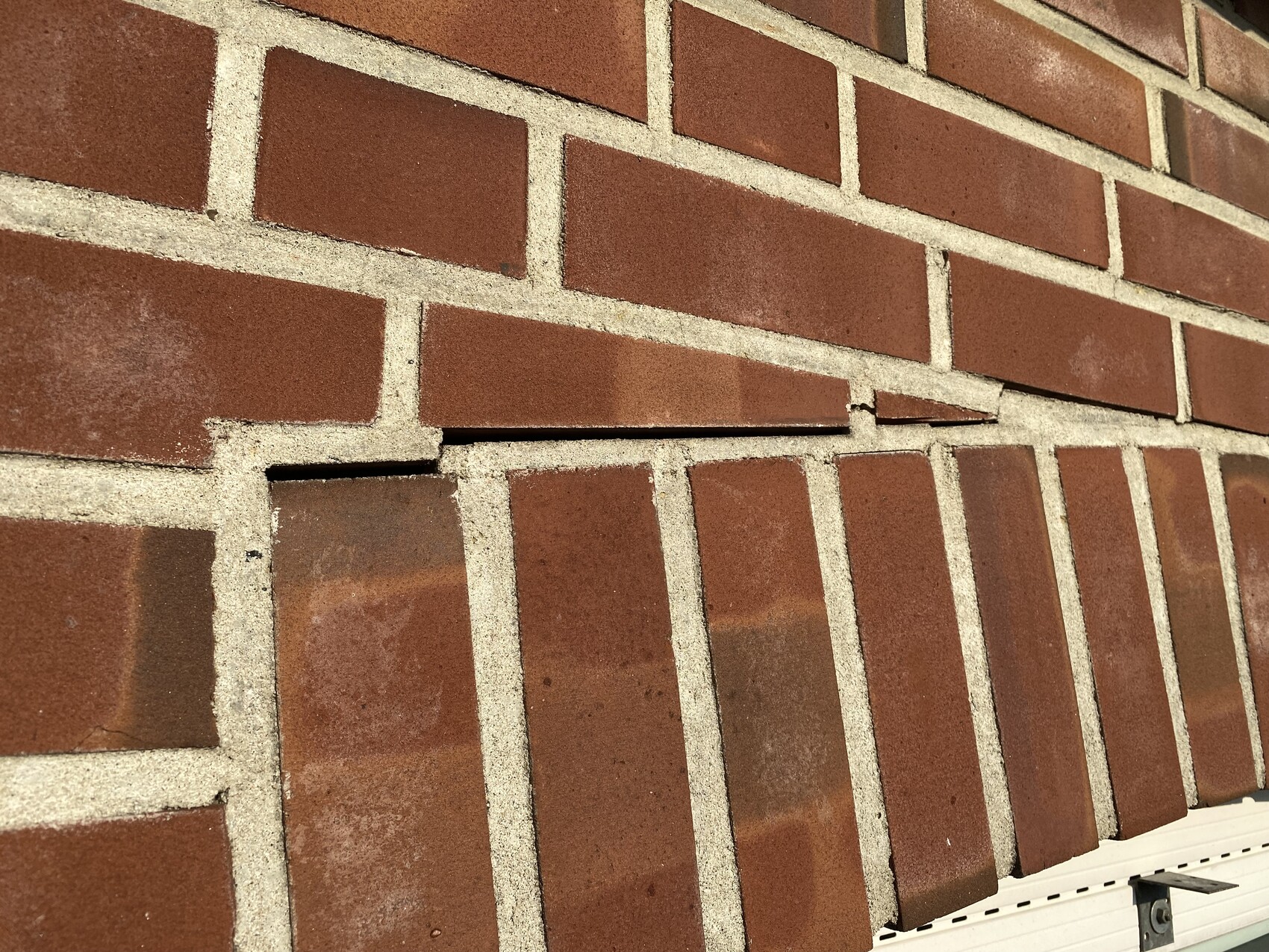 Red brick wall with damage: one brick protrudes at an angle, mortar visible.