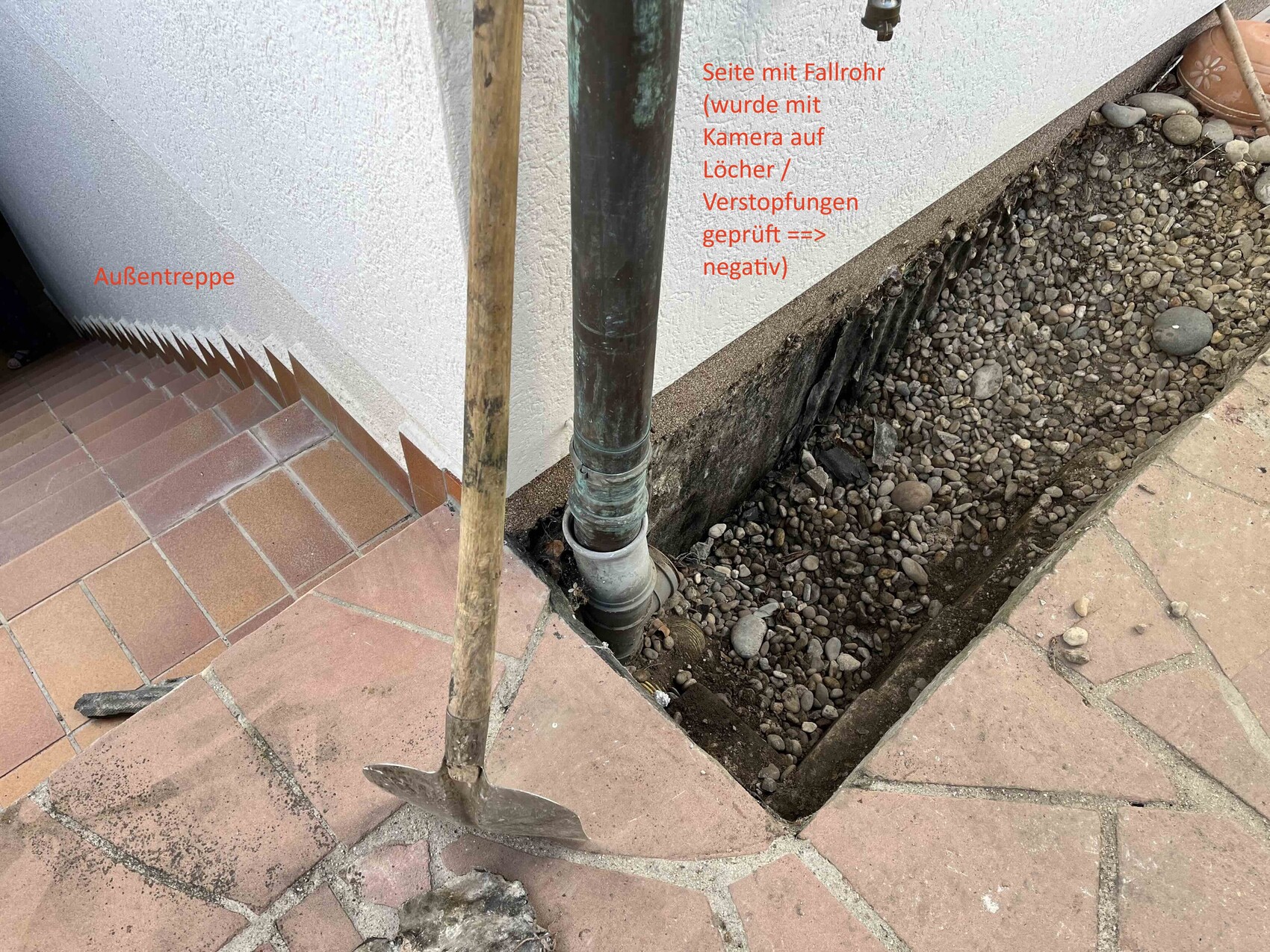 Exterior stairs on the left, downpipe on the masonry, trench with gravel and a shovel in front
