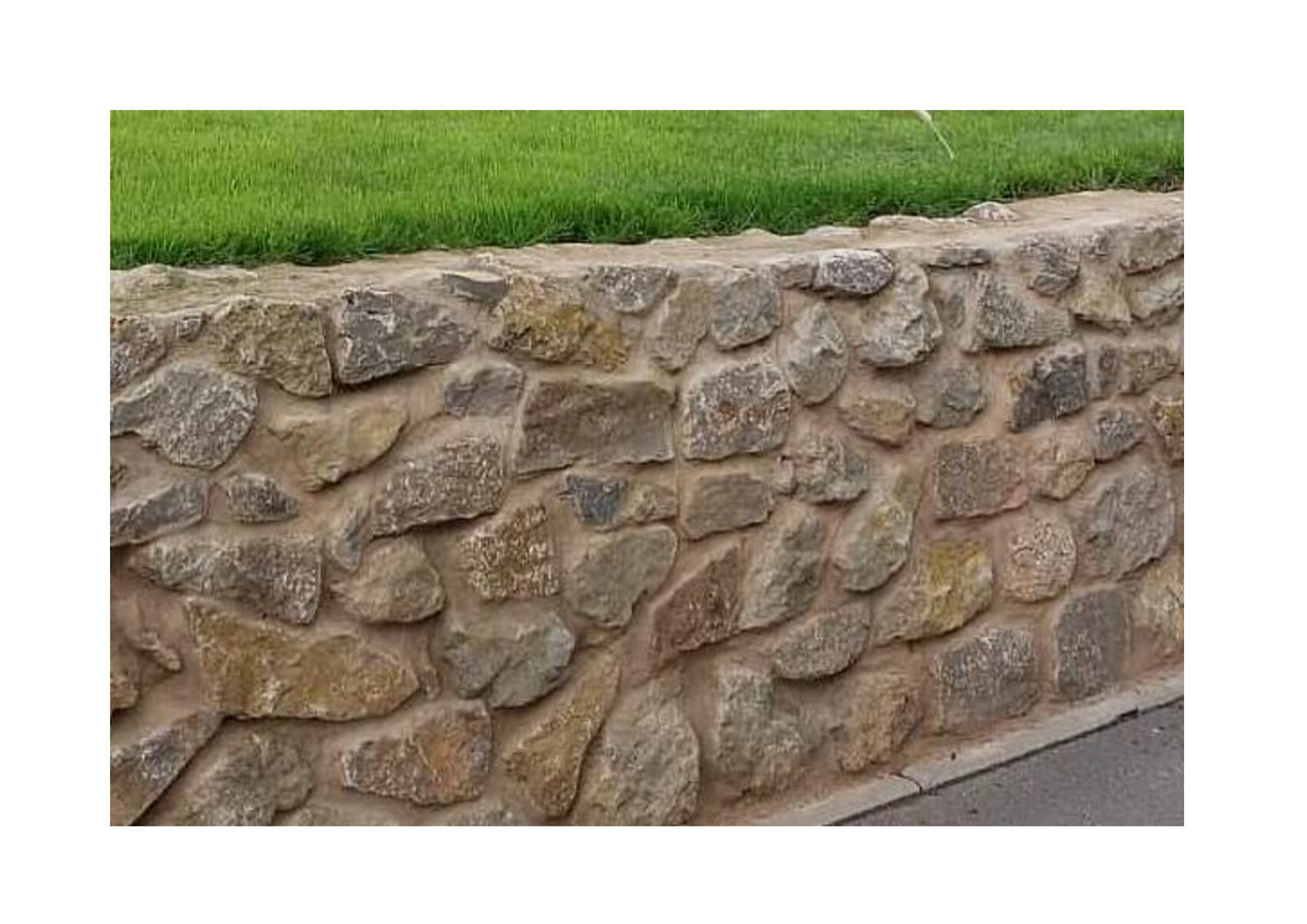 Natural stone wall at the grass edge next to garden walkway