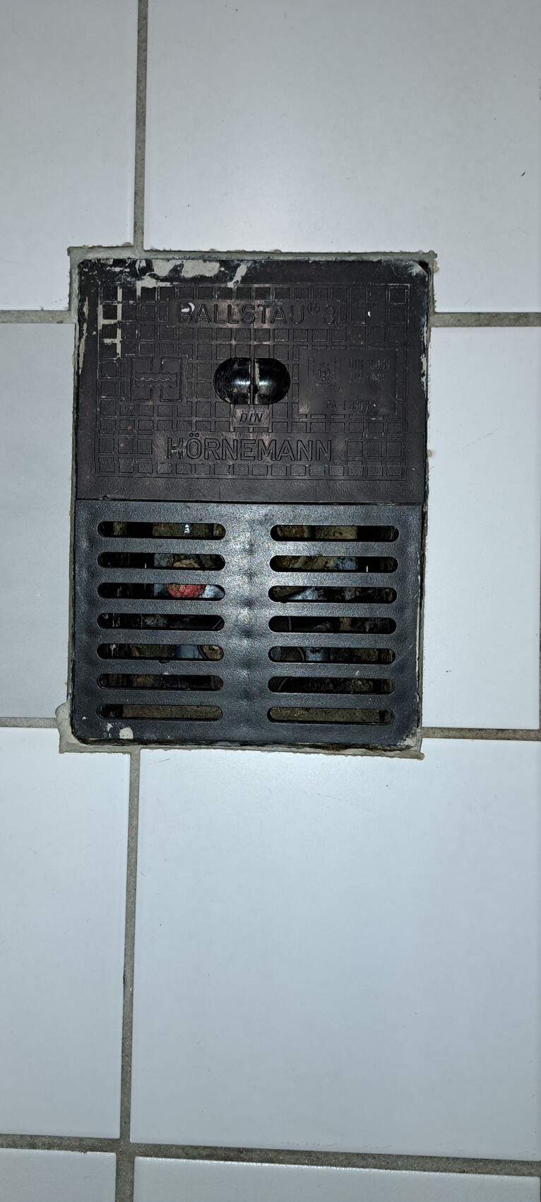 Metal floor drain cover with horizontal ventilation slots in tiled floor; HÖRNEMANN
