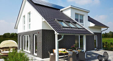 Modern white house facade with dark stone-look, terrace, and garden.