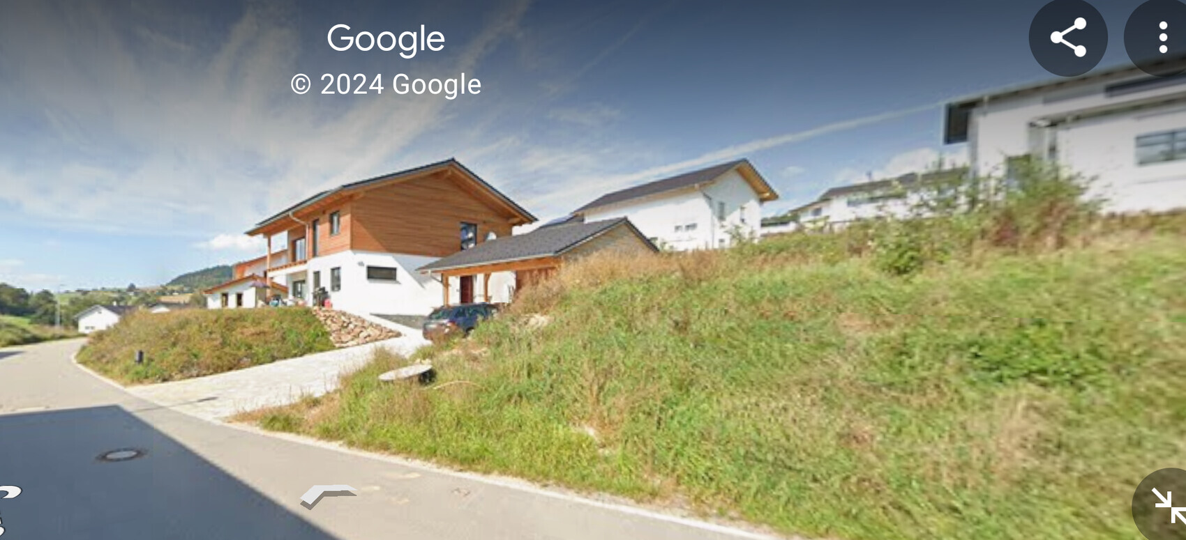 Residential houses on a slope along a winding road, green meadow and blue sky.