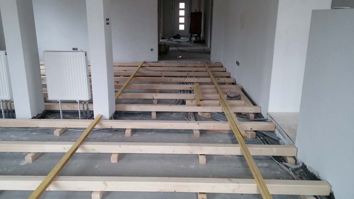 Rohbau-Innenraum: Boden aus Holzbalkenkonstruktion, Radiator links, Flur mit Tür am Ende.