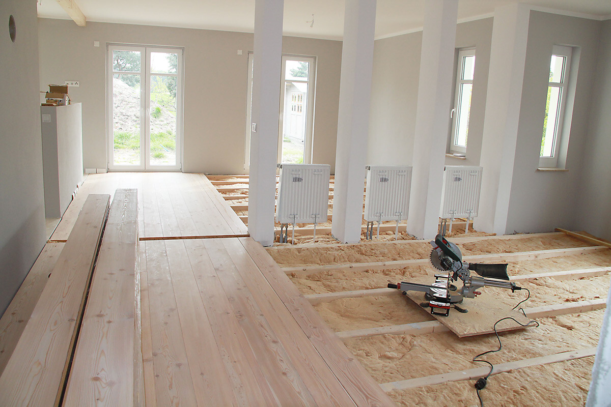 Baustellenraum mit Holzplankenboden, freigelegten Balken, Säge und Heizkörpern.