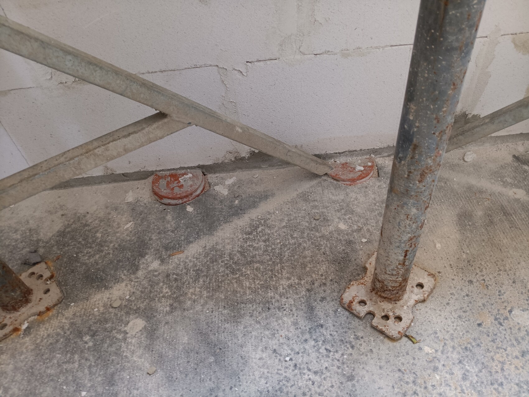 Rusty metal scaffolding supports on concrete floor in front of white wall.