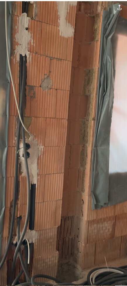 Red brick exterior wall in shell construction with cables, plaster remnants, and plastic sheeting