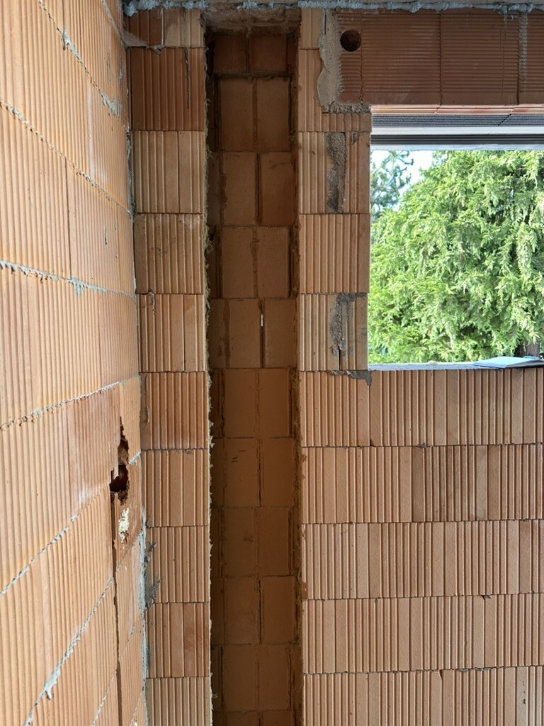 Shell construction made of brick, vertical wall opening, view outside to green trees.