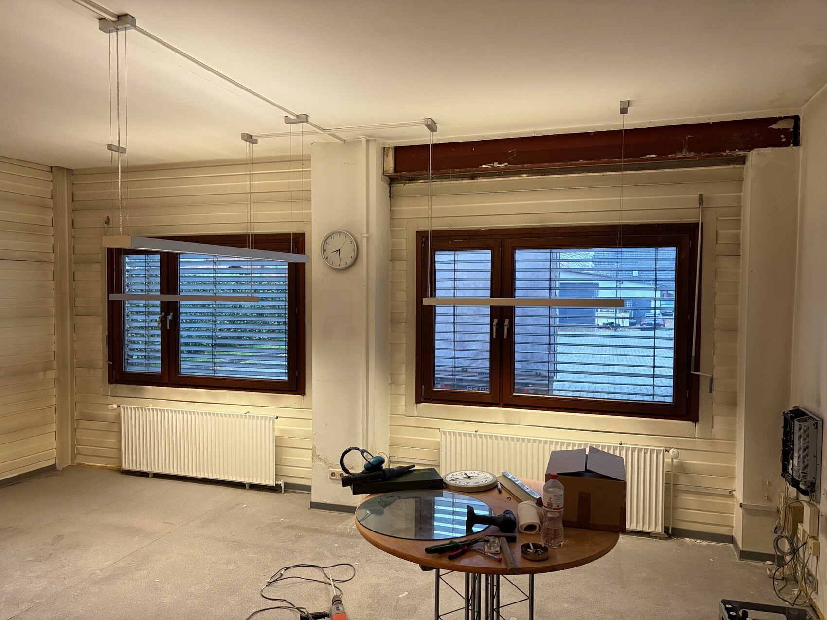 Renovated interior with two wooden windows, pendant lamps, and a table full of tools.