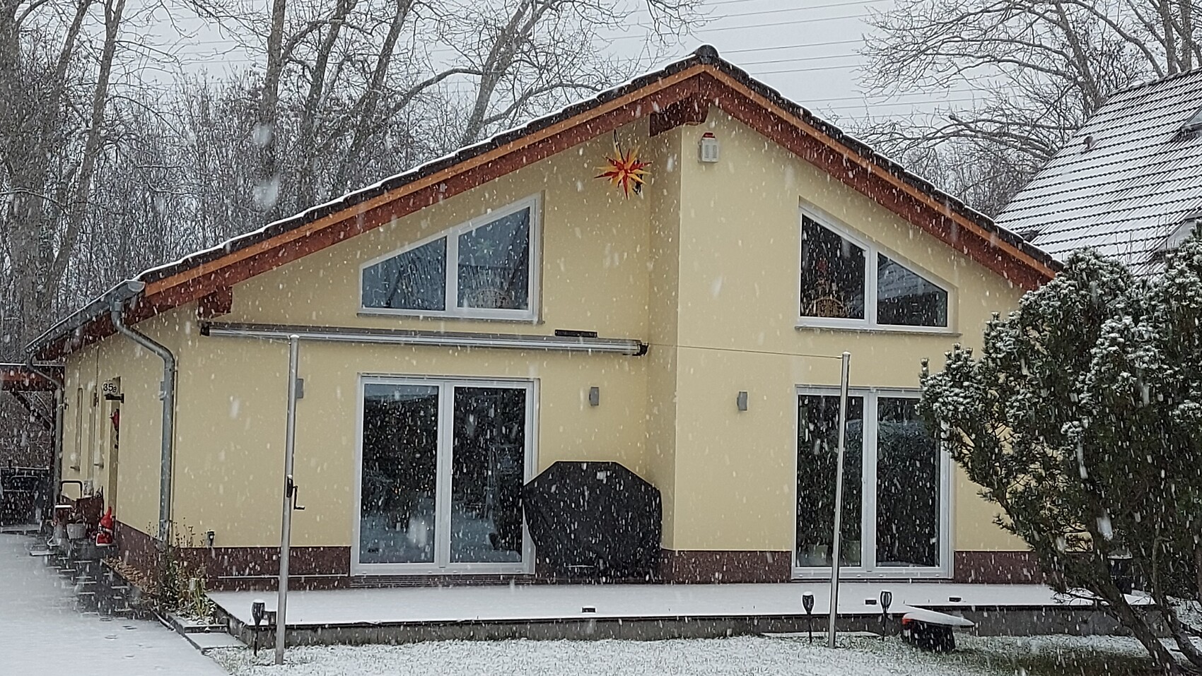 Yellow detached house with terrace, snow falling, covered grill, and star decorations.