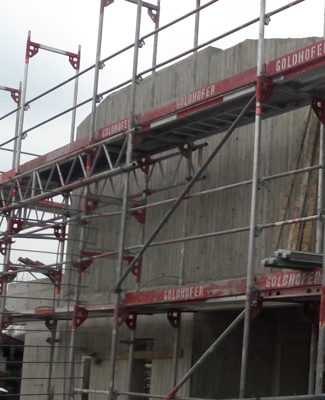 Steel scaffolding in front of a concrete wall; red scaffolding with Goldhofer lettering.