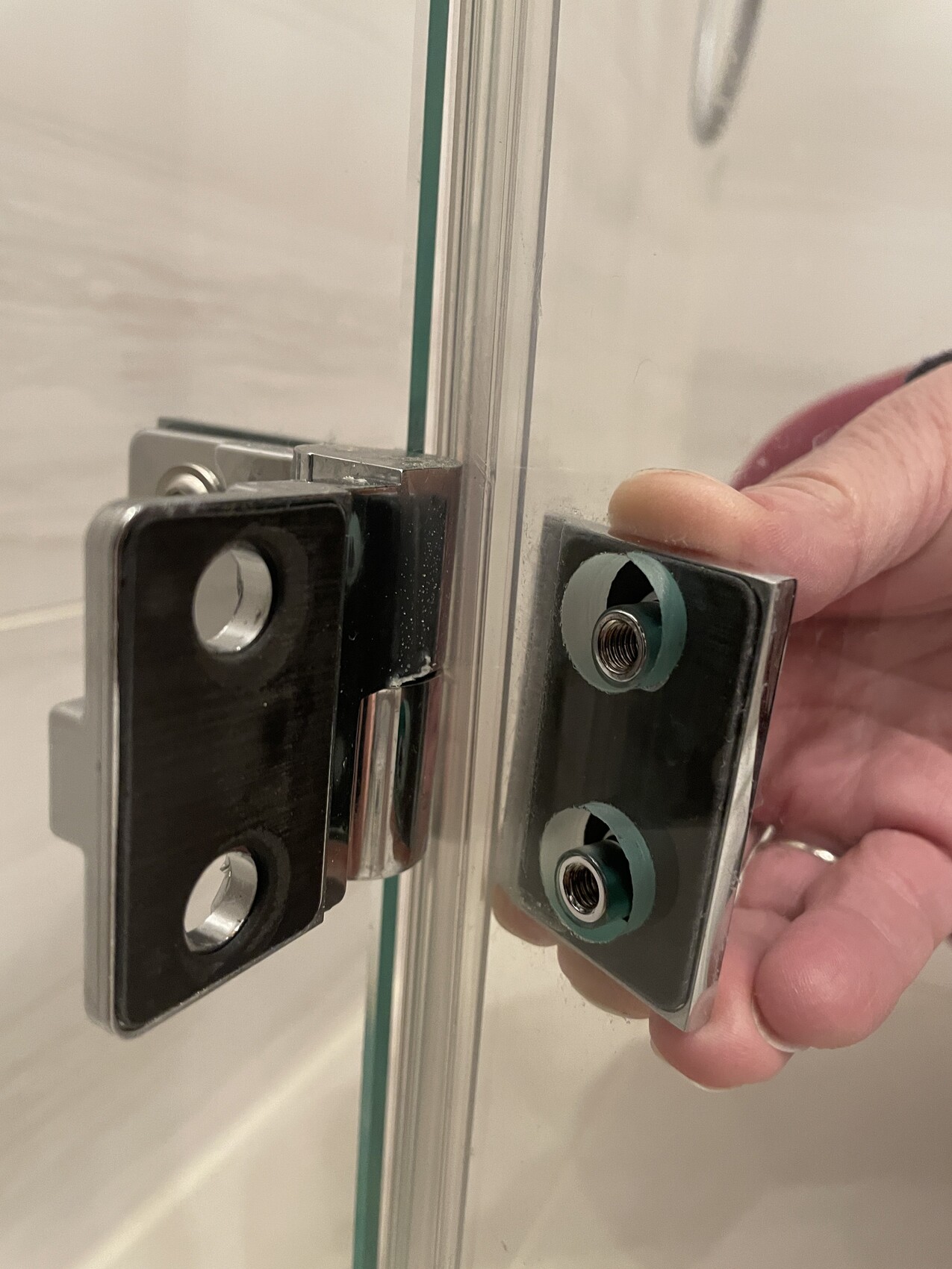 Close-up of a pair of shower glass hinges: metal plates with threaded sockets, hand assembling.
