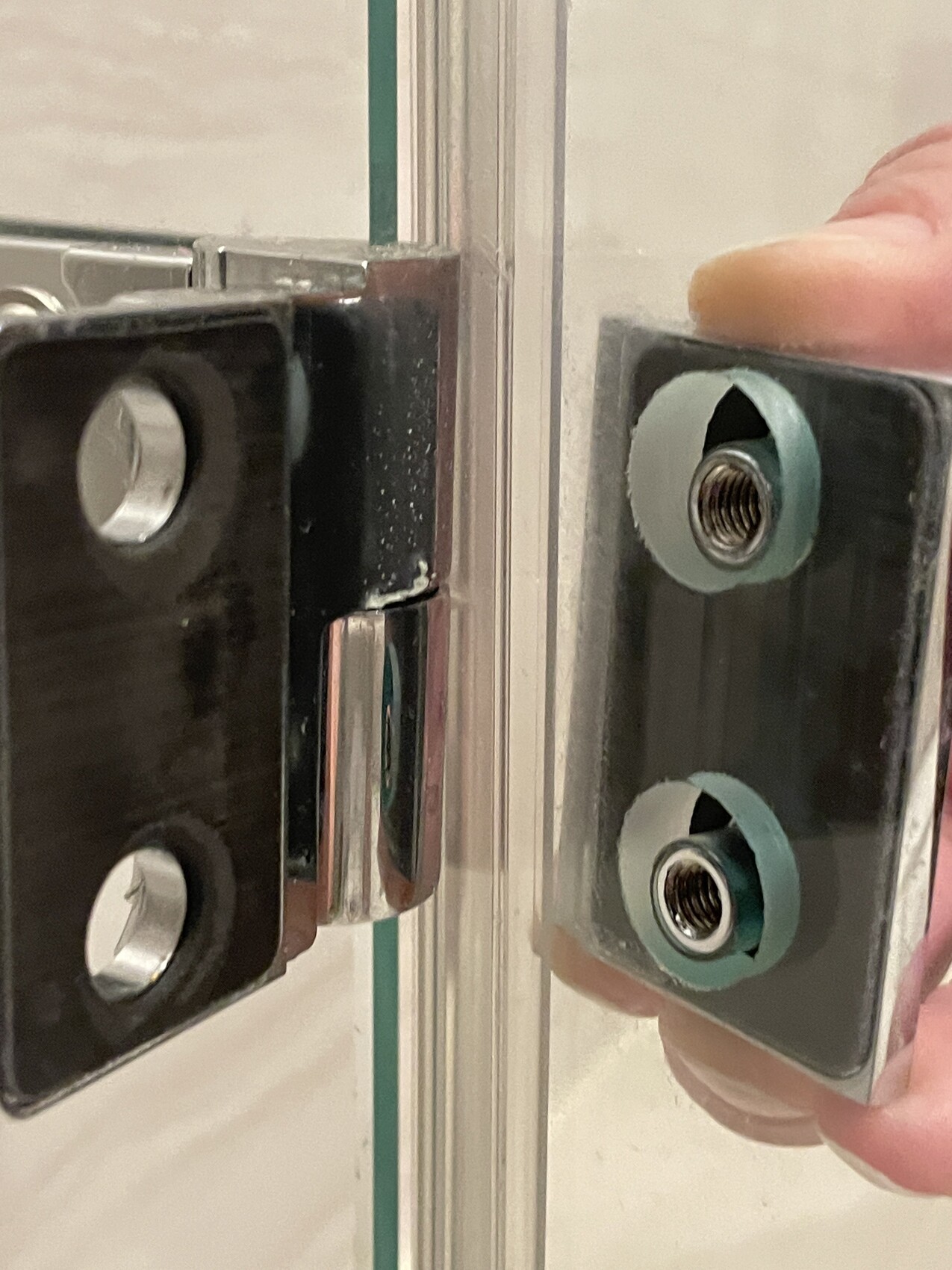 Close-up of a glass door fitting: left black component, right plate with threads.