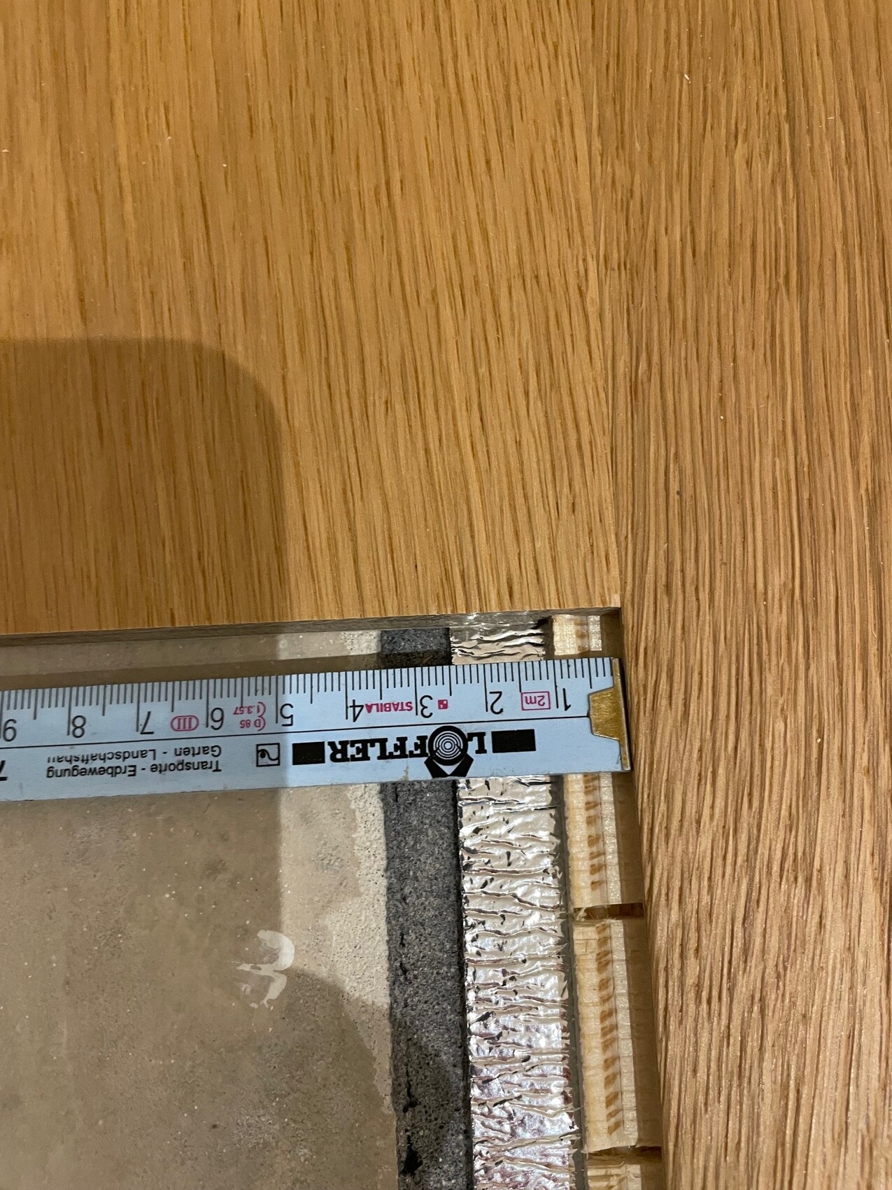 Measuring tape laid across a wood surface next to an edge of aluminum foil and insulation material.