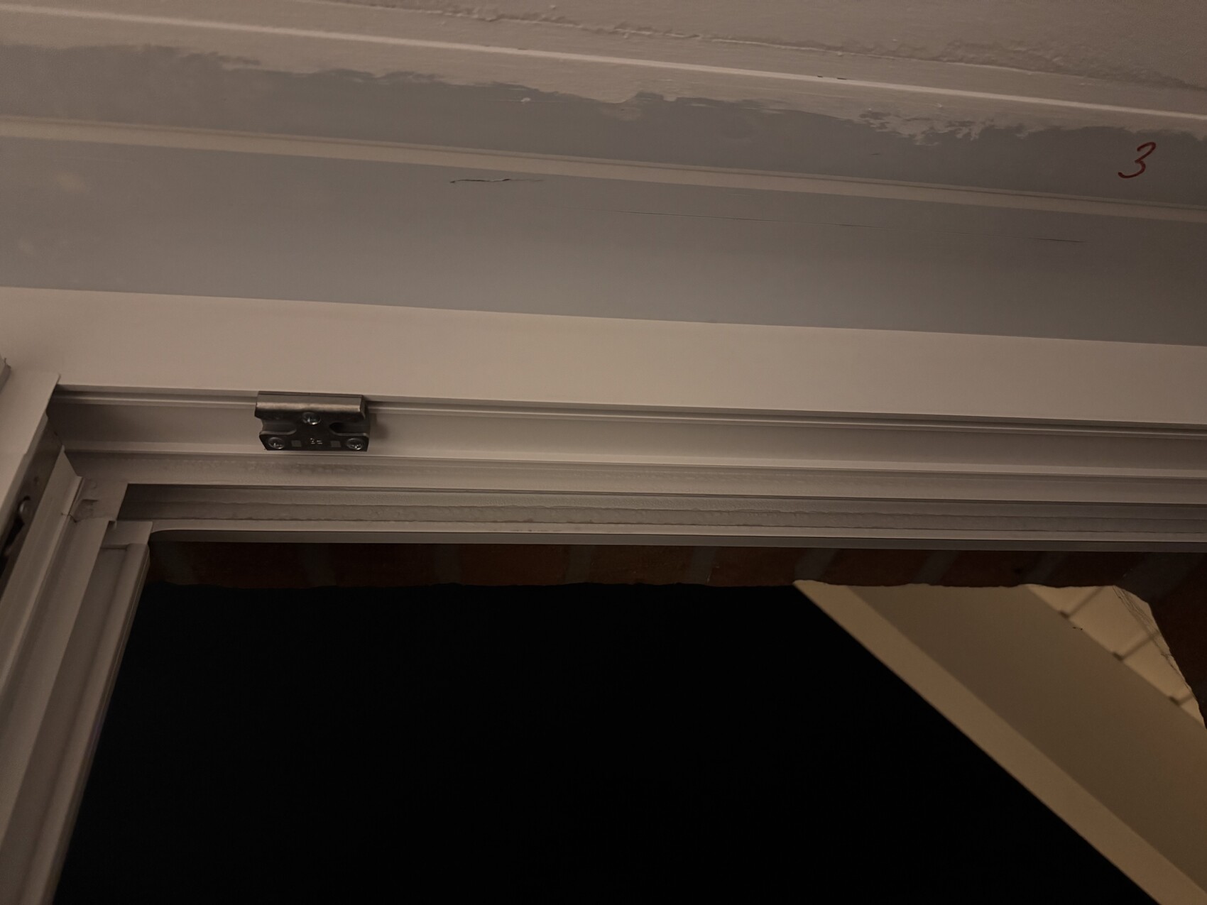 Door frame with sliding door track and visible roller guide; wall with red 3.