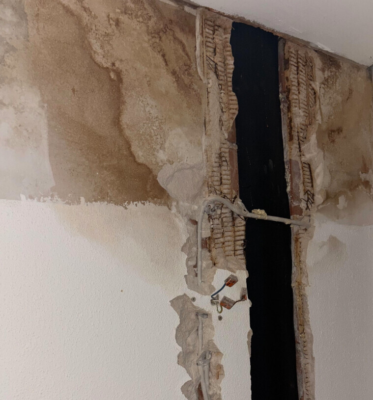 Exposed wall opening with bricks, plaster remnants, loose cables, and a dark gap behind
