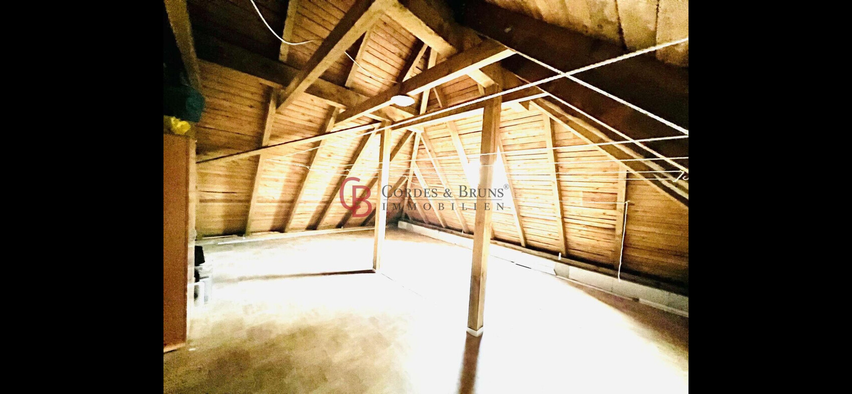 Dachboden mit sichtbaren Holzbalken und Sparren, zentrale Stütze, hell beleuchtet.