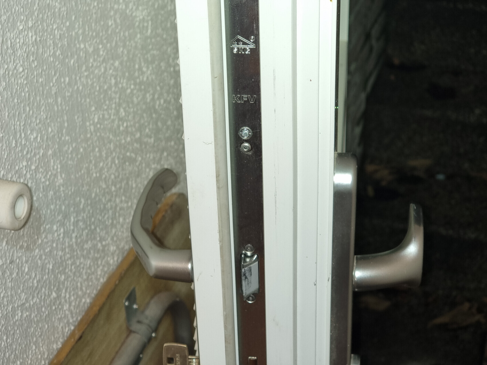 Close-up of a white door frame with a vertical metal strike plate and handle