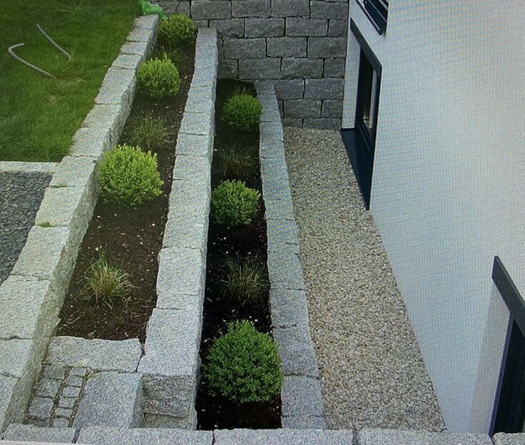 Gartenanlage mit Steinmauern, Kiesweg und Bepflanzung am Haus
