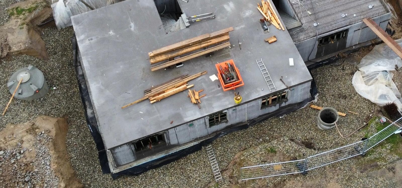 Baustellenszene auf Flachdach: Holzbretter, Werkzeugkasten, Leiter, Betonrohr und Absperrung.