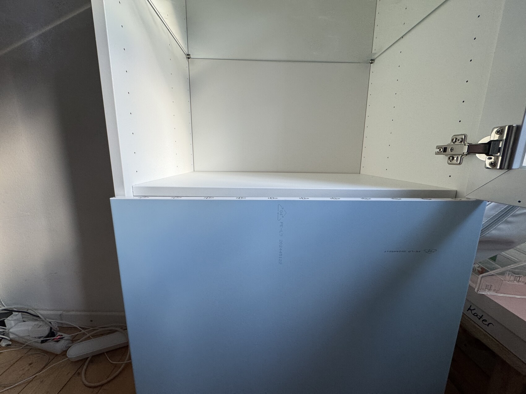 Offenes weißes Schränkabinett mit blauer Front, leerem Innenraum, sichtbares Türscharnier rechts.