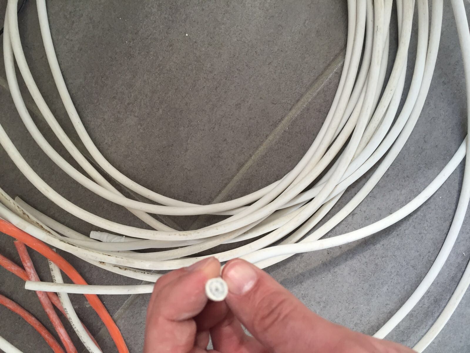 Close-up: Hand holding white cable end; many white cables, orange cables lying on the floor.