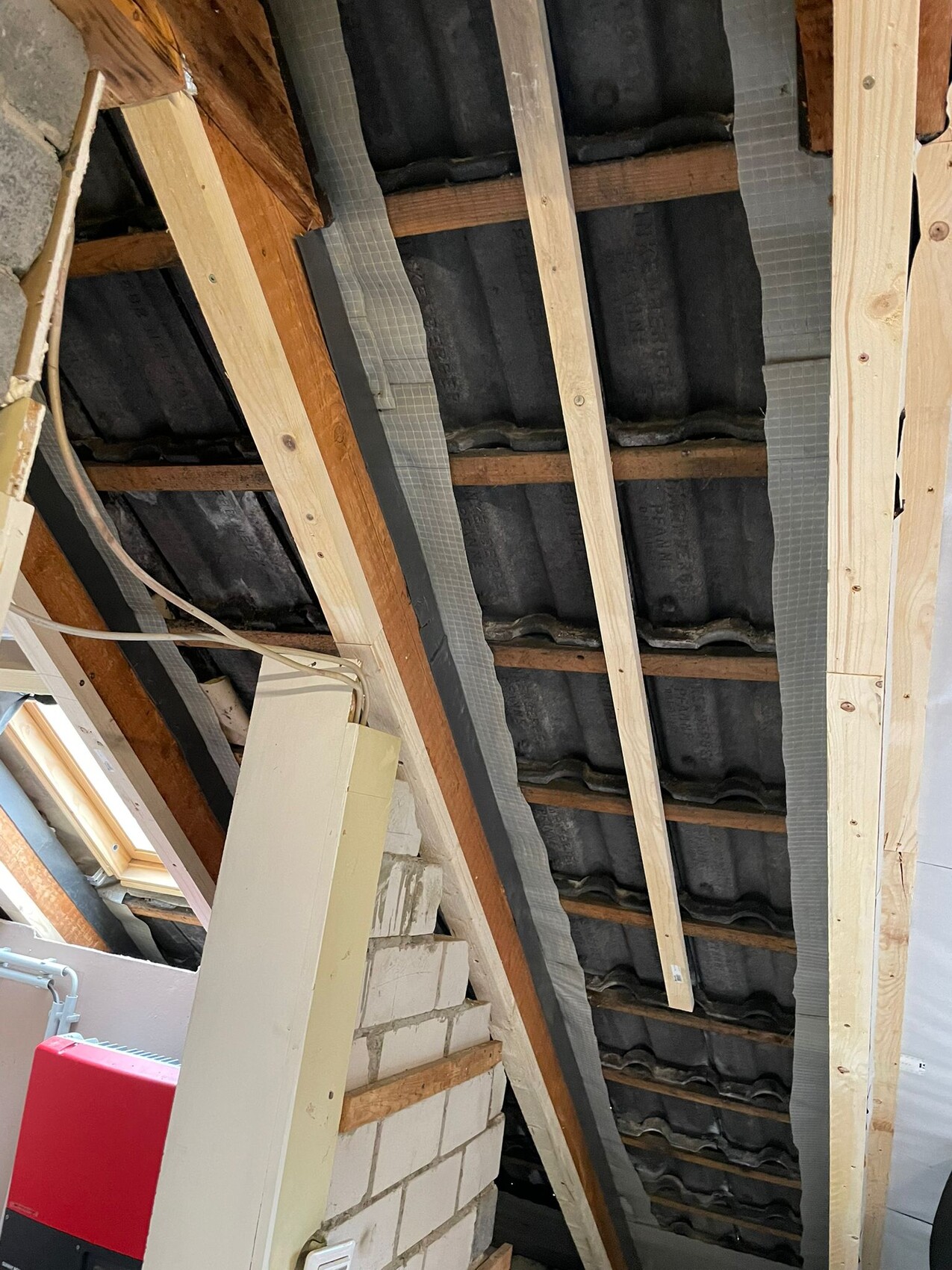 Attic with exposed rafters, dark roof tiles, and electrical wiring.