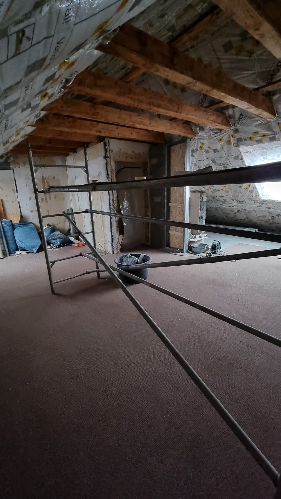 Attic rough construction: scaffolding in room, insulation on roof and walls, building materials and tools.