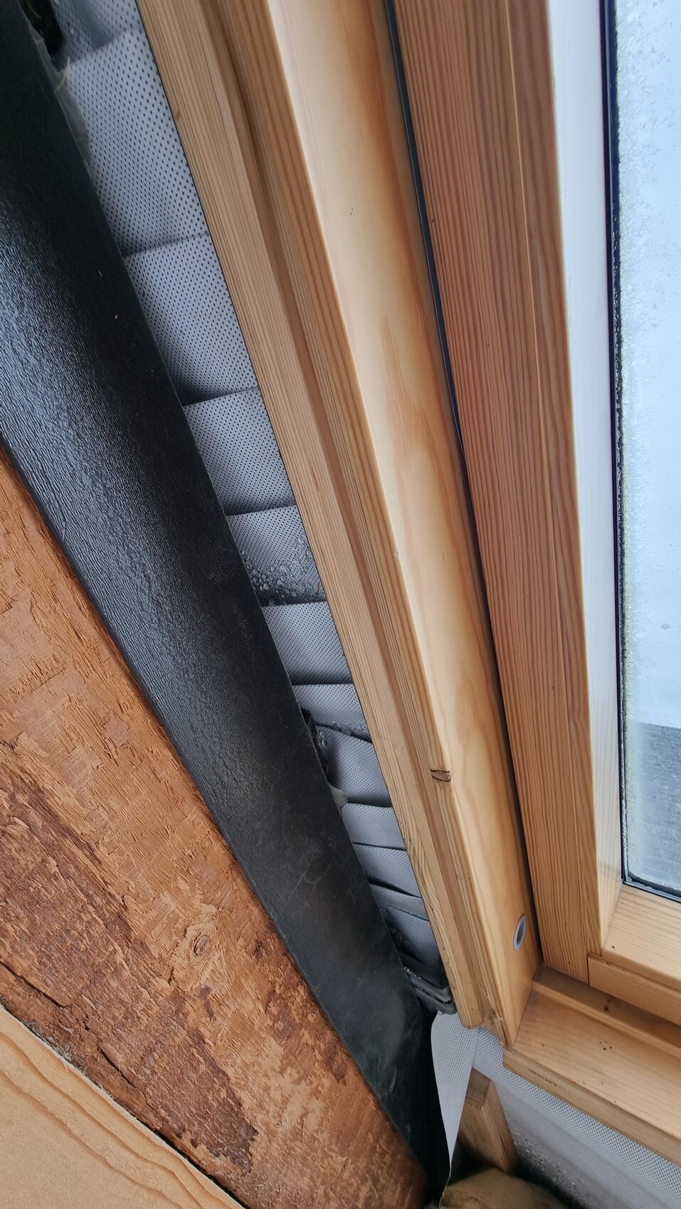 Close-up of wooden window frame with glass, sealing, and insulation material at the edge.