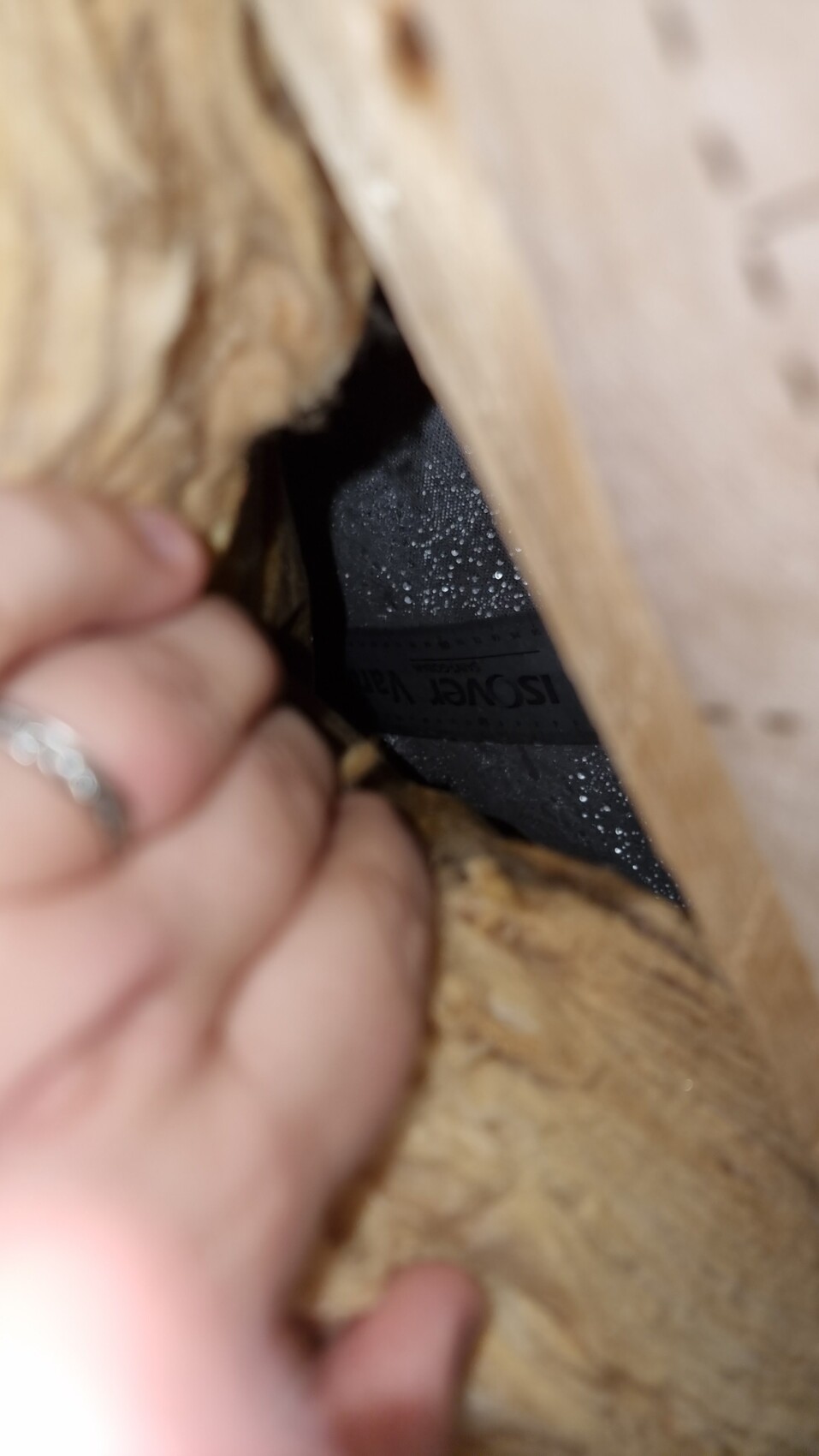 Hand pulling Isover insulating material out of wall opening behind wooden frame.