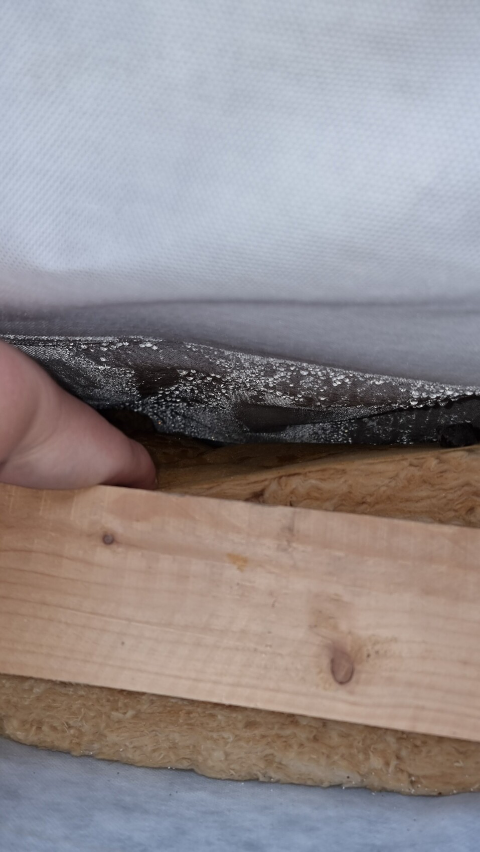 Hand lifting vapor retarder over mineral wool insulation between wooden battens.