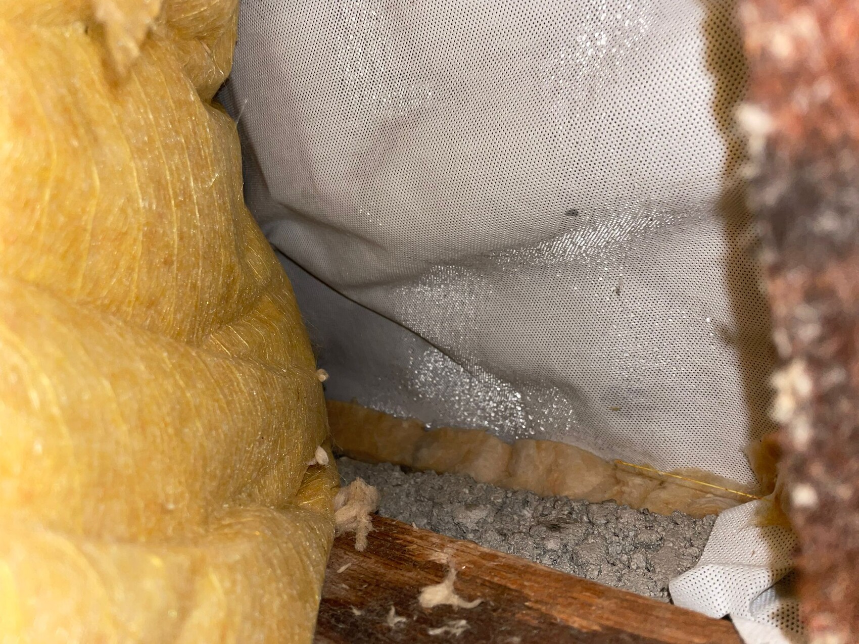 Interior side of wall/ceiling with yellow glass wool insulation, grey vapor retarder, and wooden beams.