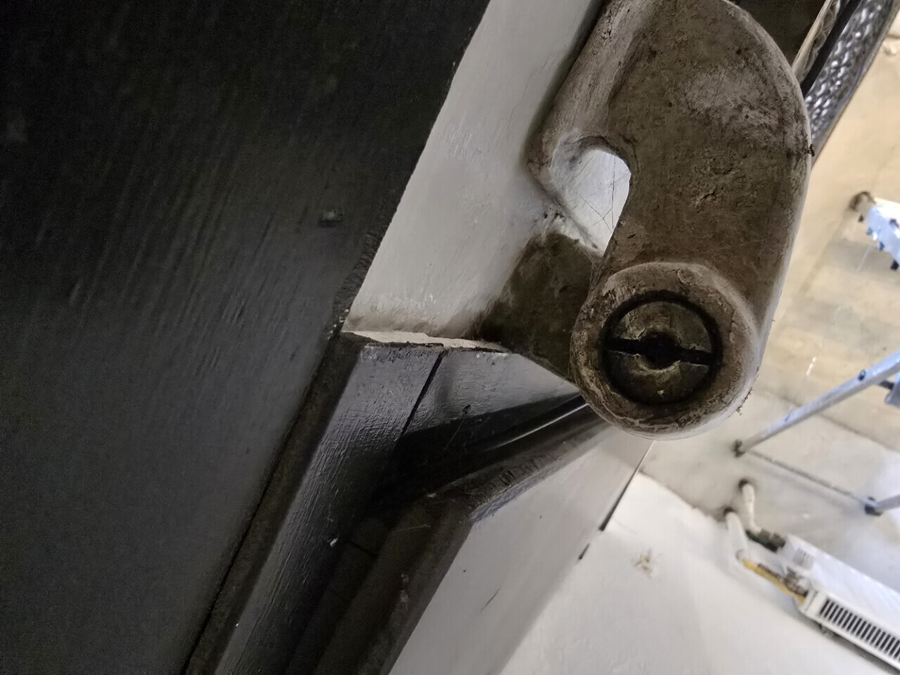 Rusty door bolt with round head and slot; mounted on a dark door frame, background construction scaffold.