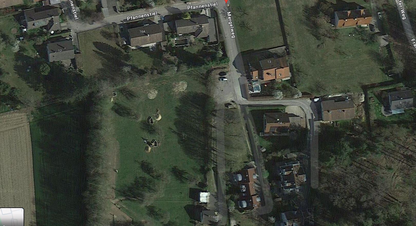 Aerial photo of a residential area: rows of houses, street intersection, gardens, and green open space on the left.
