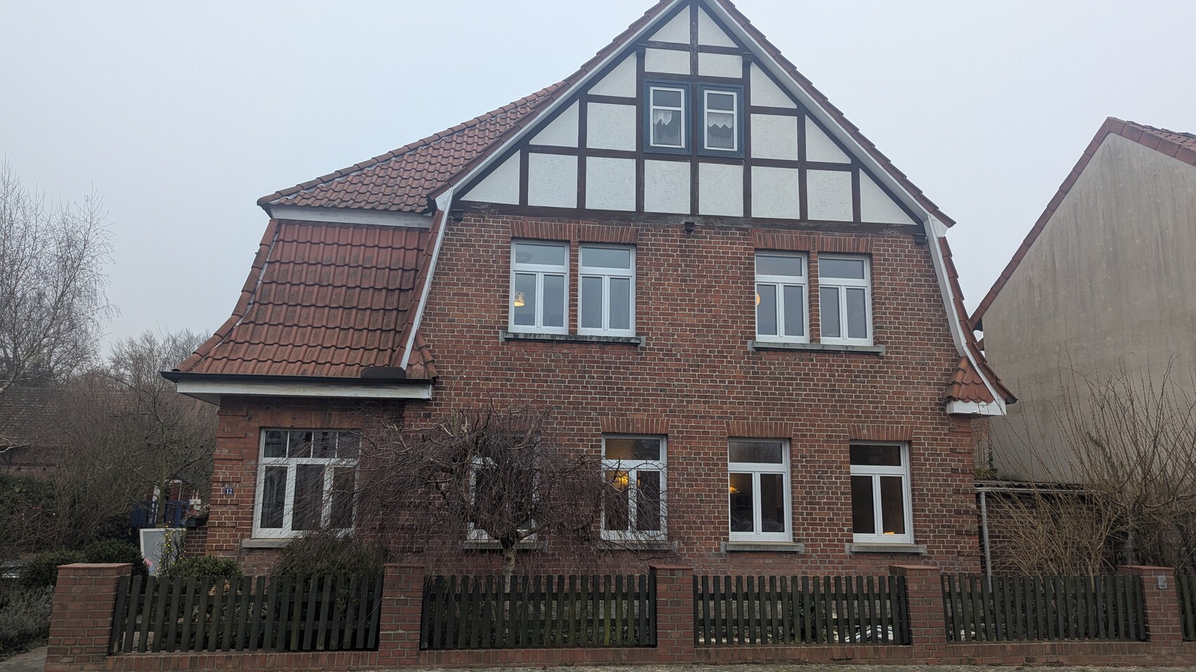 Exterior view of a red brick house with a timber-framed gable, white windows, and fence